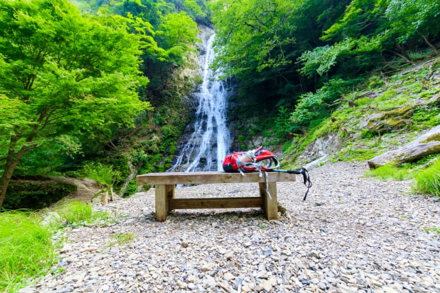 滝の前のベンチに置かれた赤いリュック。滝行の持ち物を準備するイメージ